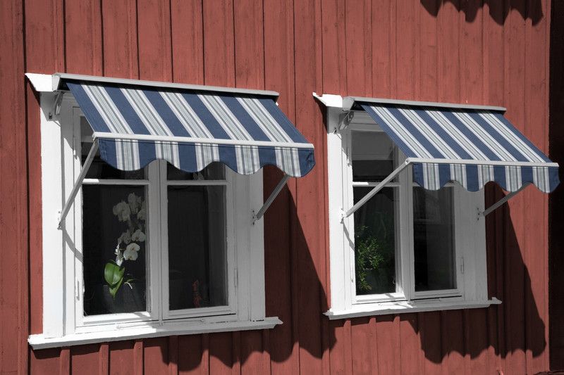 Randig markisväv i blått, grått och vitt på ett falurött hus