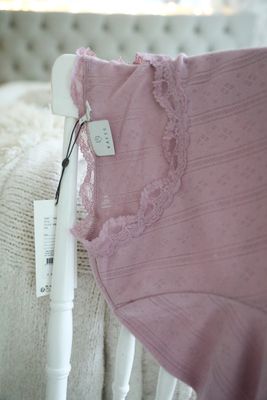 Nahaufnahme eines lilarosa, pointillistisch gestrickten Stoffes mit kleinen Lochmustern und einer verspielten Spitzenbordüre