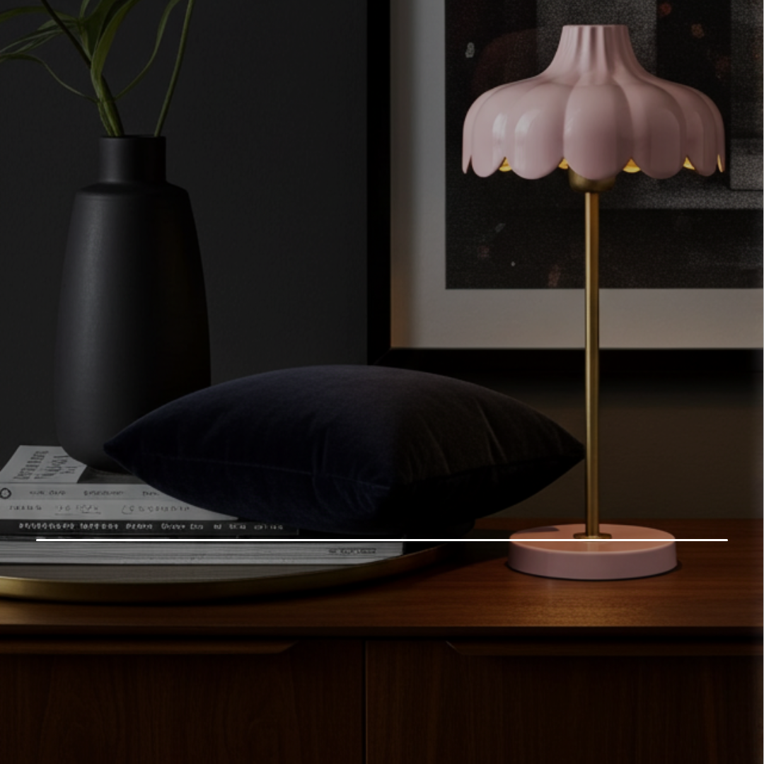 Rosa bordslampa med blomformad skärm och mässingsstativ på teaksideboard, mörkblå sammetskudde och svart vas i bakgrunden