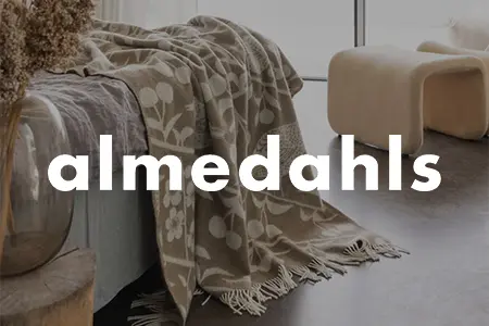 Mönstrad pläd från Almedahls med blommor och cirklar i neutrala toner, draperad över en soffa i ett ljust rum med naturligt ljus.
