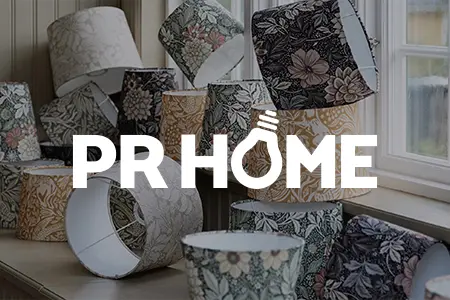 Lampskärmar med botaniska mönster från PR Home i olika färger, arrangerade på träbord vid fönster i ljus inredningsmiljö.