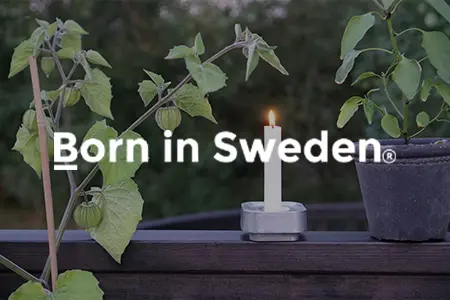 Metallisk ljushållare från Born in Sweden på mörkt träbord bredvid tomatplantor i grönskande trädgårdsmiljö.