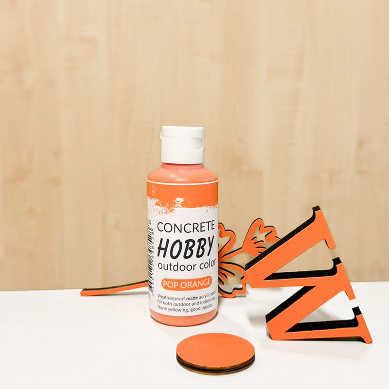 Färgen Pop Orange i serien Concrete Hobby Outdoor Color från Cria. På bilden har vi målat upp ett W, en cirkel och en träblomma med färgen.