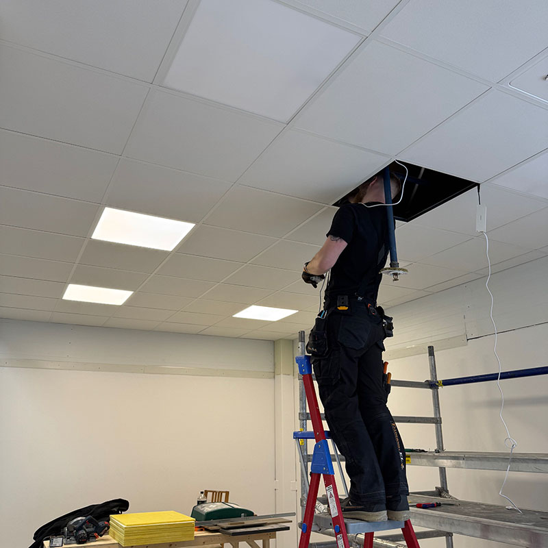 Belysning kommer på plats i vår nya butik. Elektrikern står på en stege och kopplar lampor.