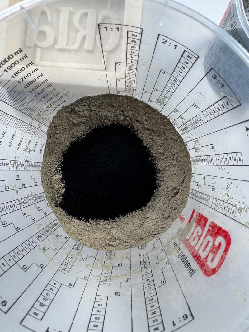 Betongpulver i ett blandkärl med extra svart färgpigment