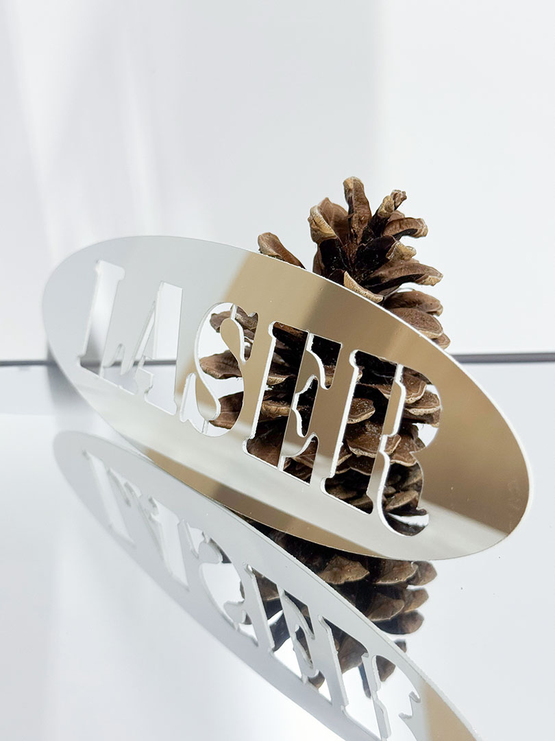 Laserskära Spegel Hips En laserskuren Spegel-Hips (spegelplast) med en kotte i bakgrunden