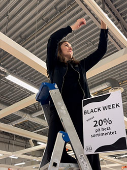 Jossan på Cria står på en stege och hänger upp Black-Friday-skyltar i butiken i Tornby