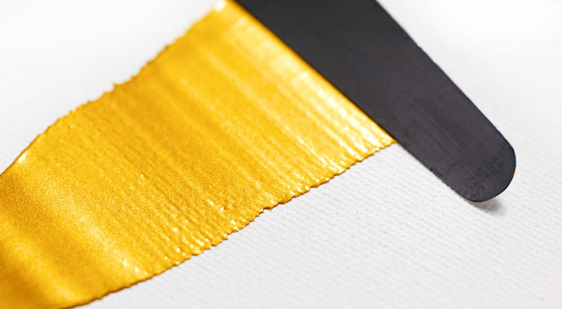 Gyllene färgstråk av Winsor & Newton Galeria Gold applicerat med palettkniv på vit duk