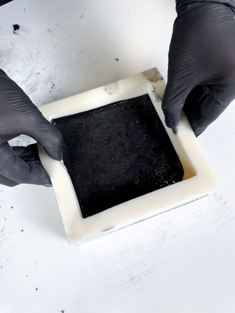 Extra svart färgpigment i silikonform hanteras med svarta handskar
