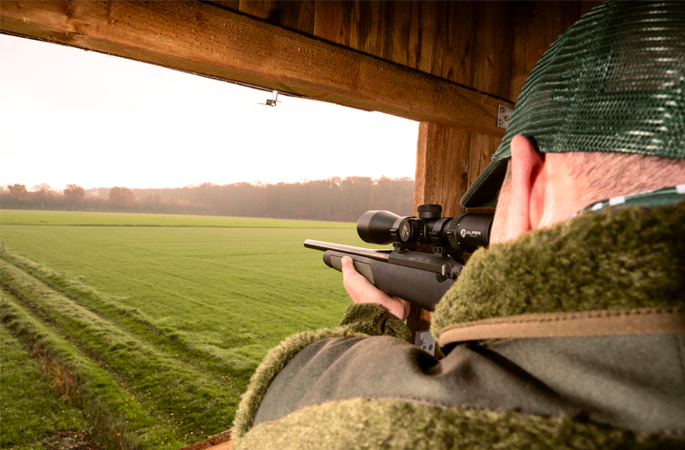 Bild på skytt som siktar över ett tomtfält med ett vapen som har ett Alpen Optics kikarsikte monterat